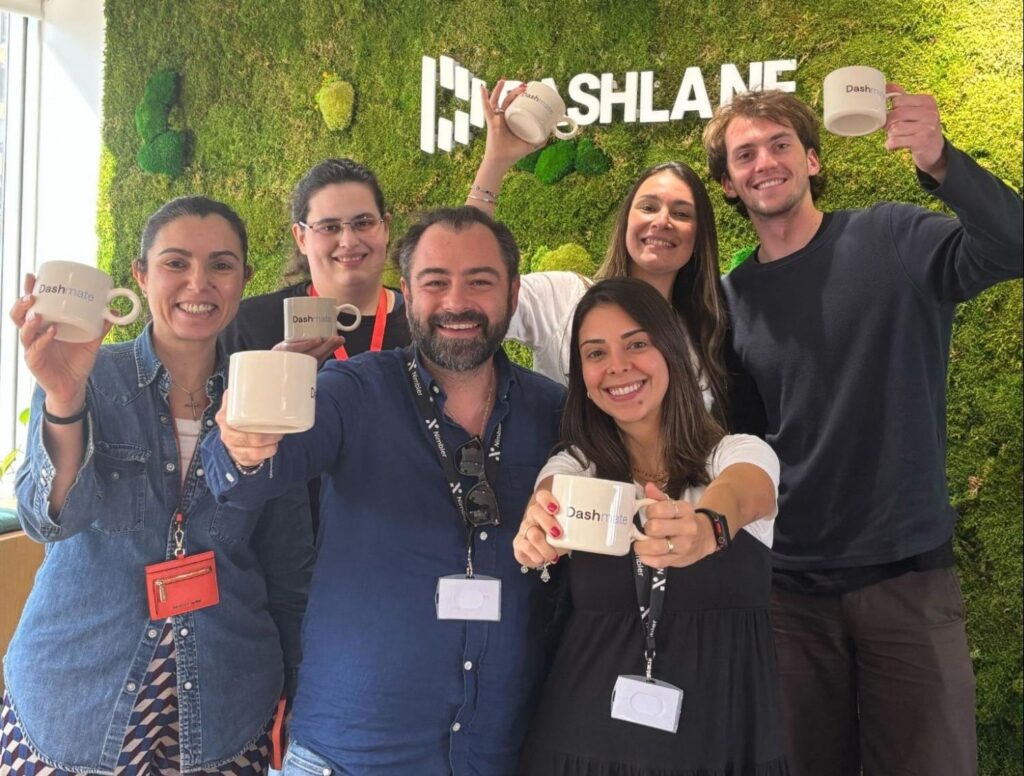 Six Dashmates holding branded mugs smile in front of the Dashlane logo.