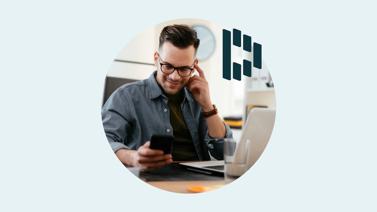 Man at a desk with a laptop who is holding a mobile device