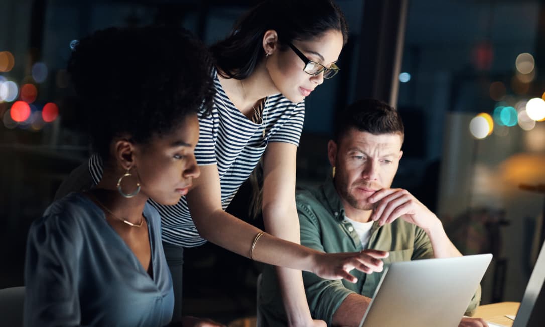 Three colleagues collaborate around a computer, representing Dashlane’s business password management product and how it secures access and boosts employee productivity.