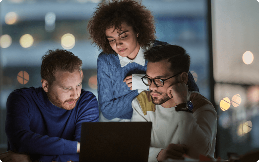 Three employees collaborate around a computer, browser activity secured by Dashlane’s risk detection.